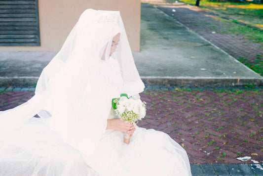 Traditional Asian bride in white dress sitting on bench.